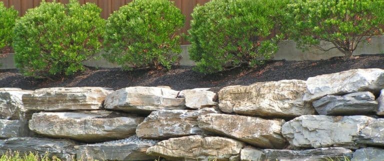 content-rock-retaining-wall-installed-beside-shrub-bed-768x323