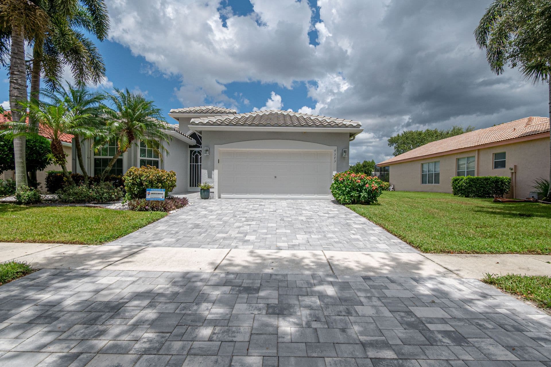 Front view of a single-story Florida home with white stucco exterior, two-car garage, paved driveway, palm trees, and landscaped yard